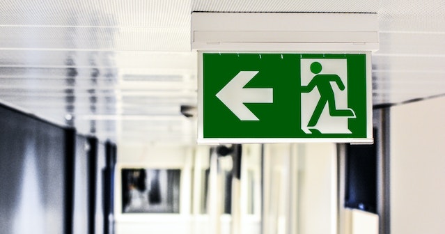 green exit sign hanging from the ceiling in hallway